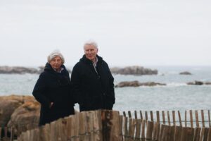 Elderly couple stands together near the ocean, enjoying a peaceful outing.